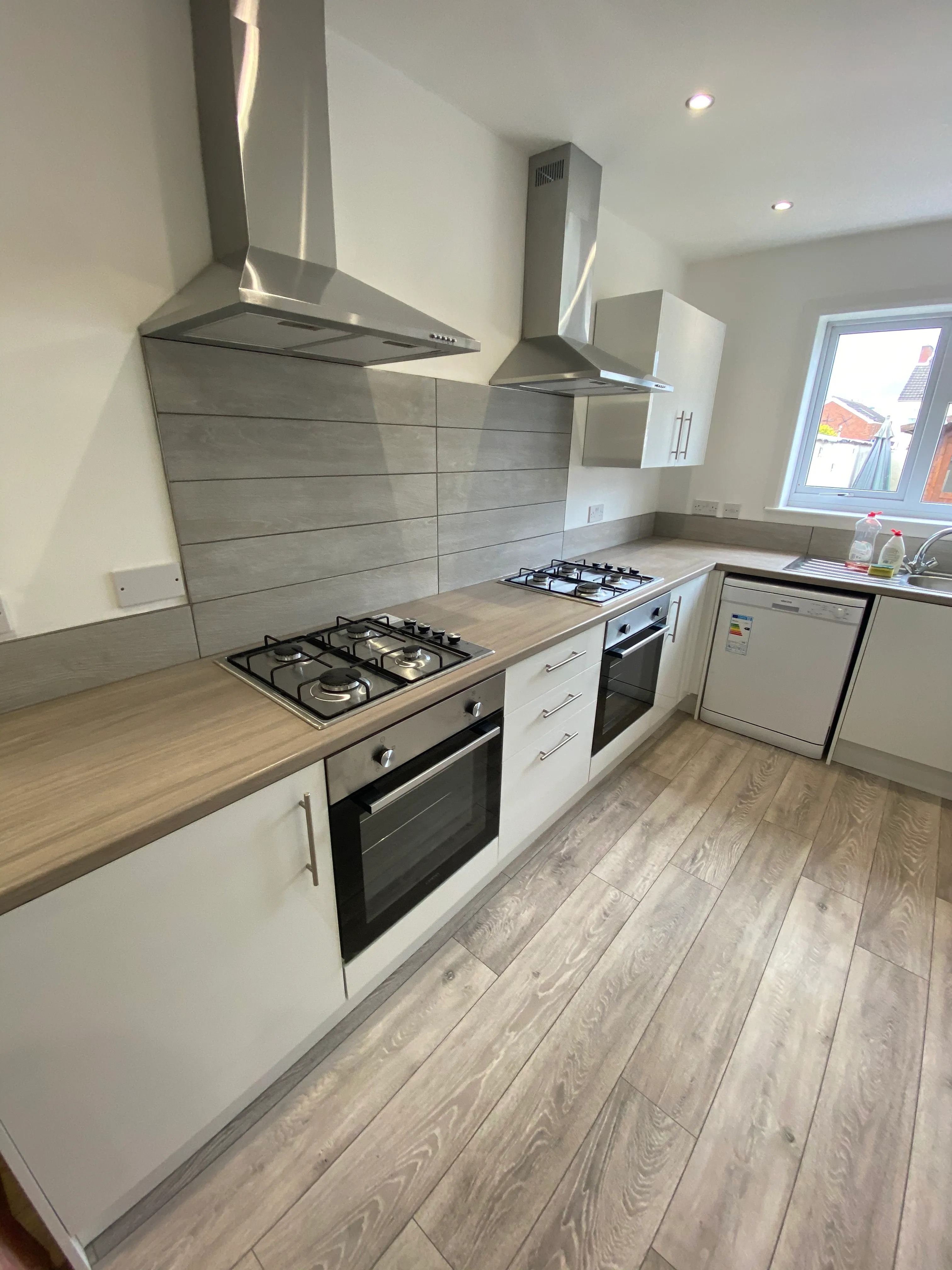 Completed kitchen refurbishment with white cabinets, grey splashback and wood-effect flooring