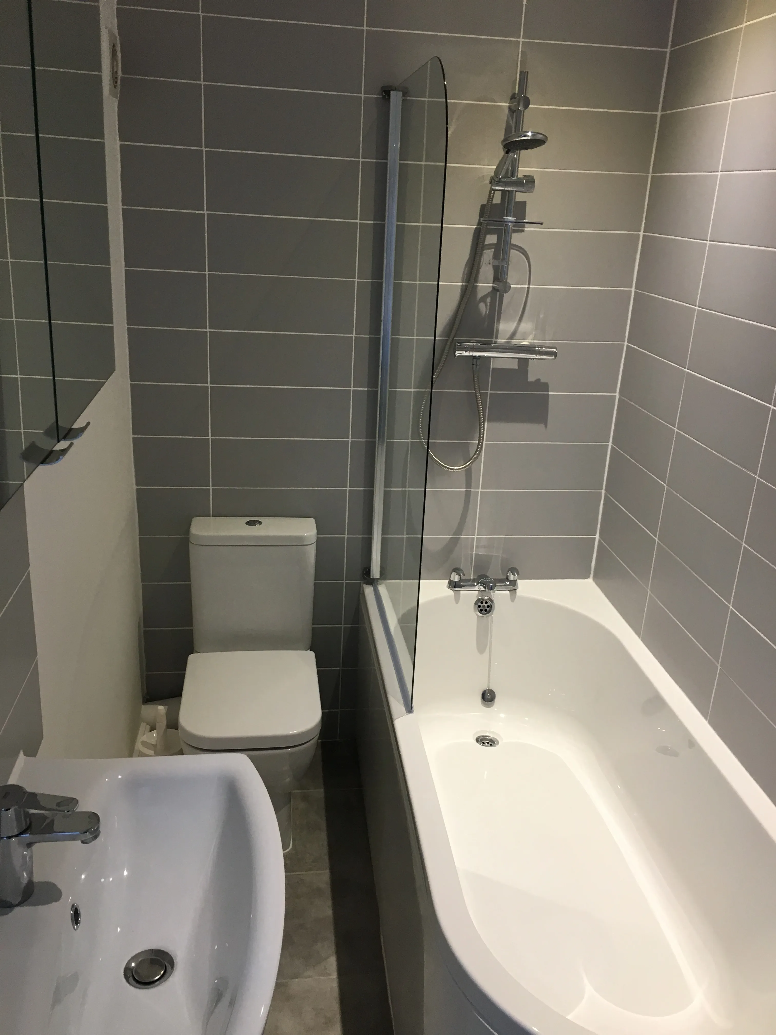Finished bathroom with grey tiled walls, bath, shower and white sanitaryware