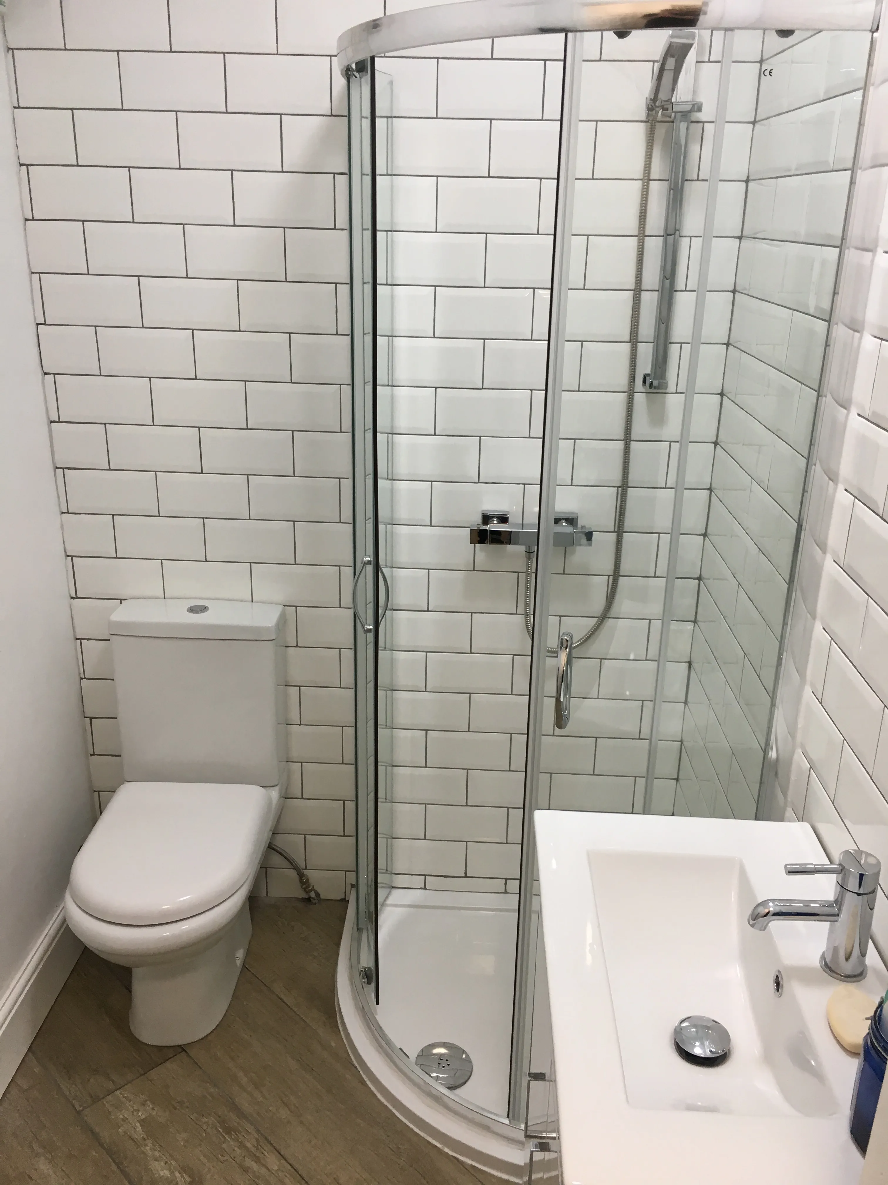 Finished bathroom with white metro tiles, curved shower enclosure and vanity basin