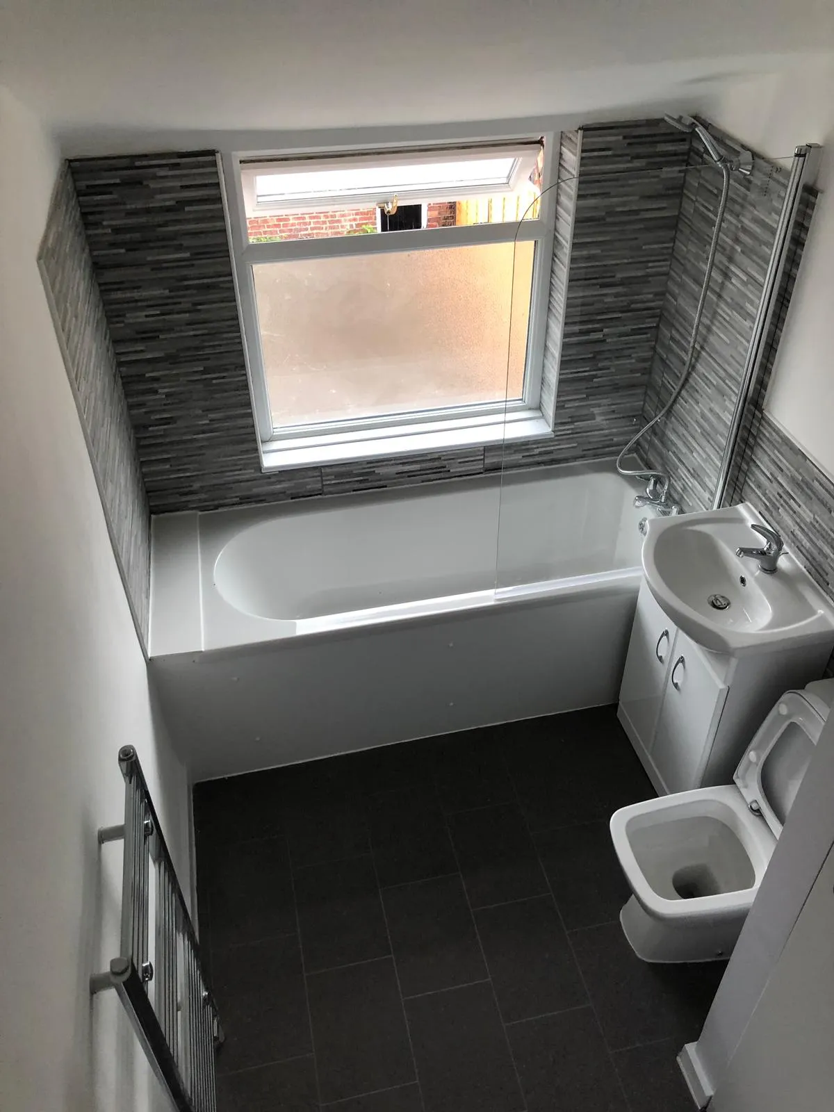 Finished bathroom with dark wall tiles, bath and white sanitaryware