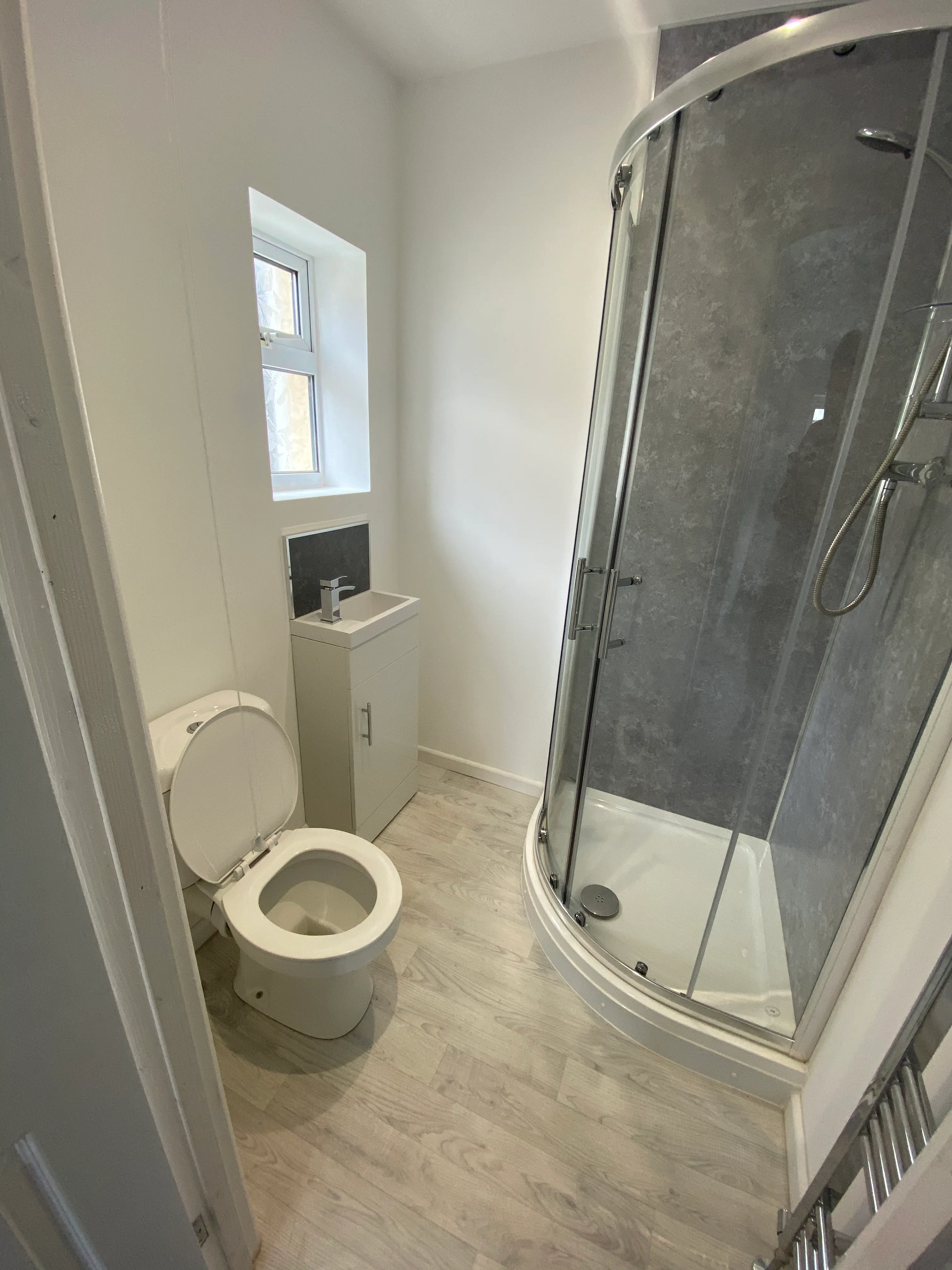 Finished bathroom with grey shower panels, white sanitaryware and light wood-effect flooring