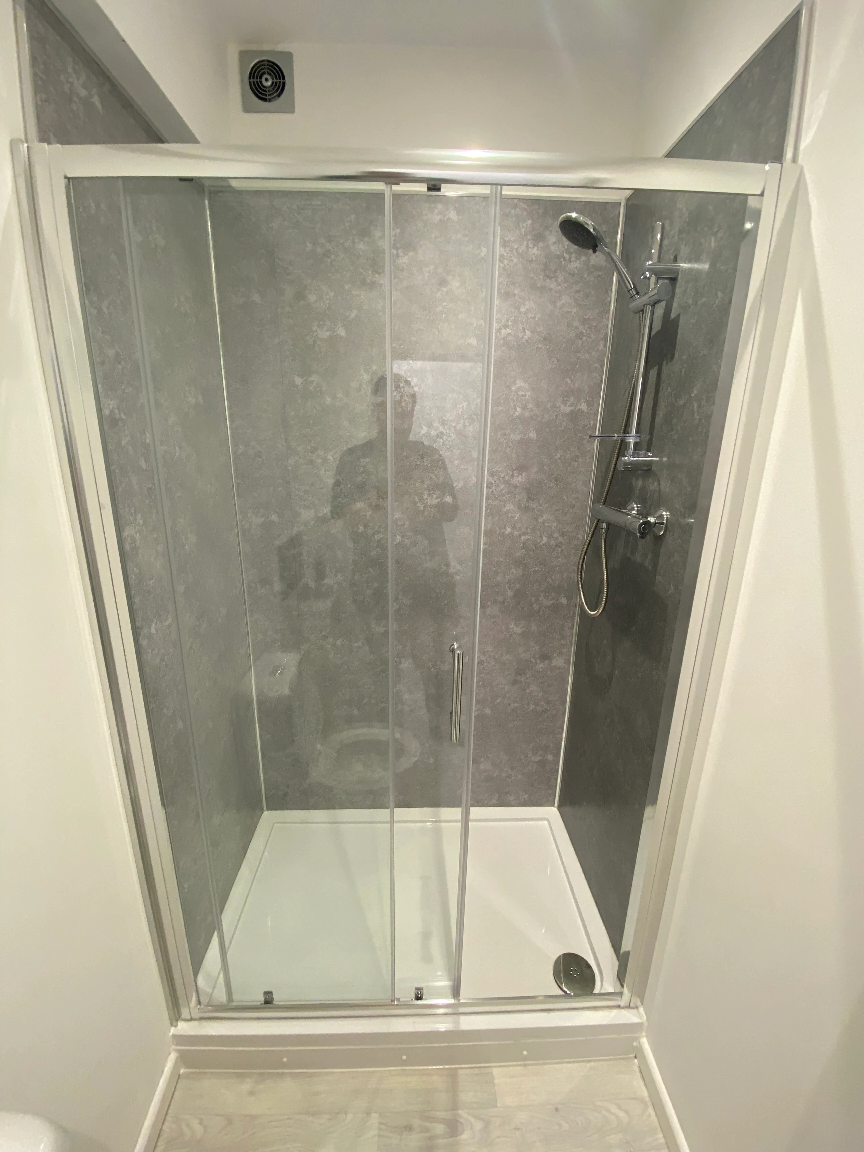 Finished bathroom shower enclosure with grey wall panels and extractor fan
