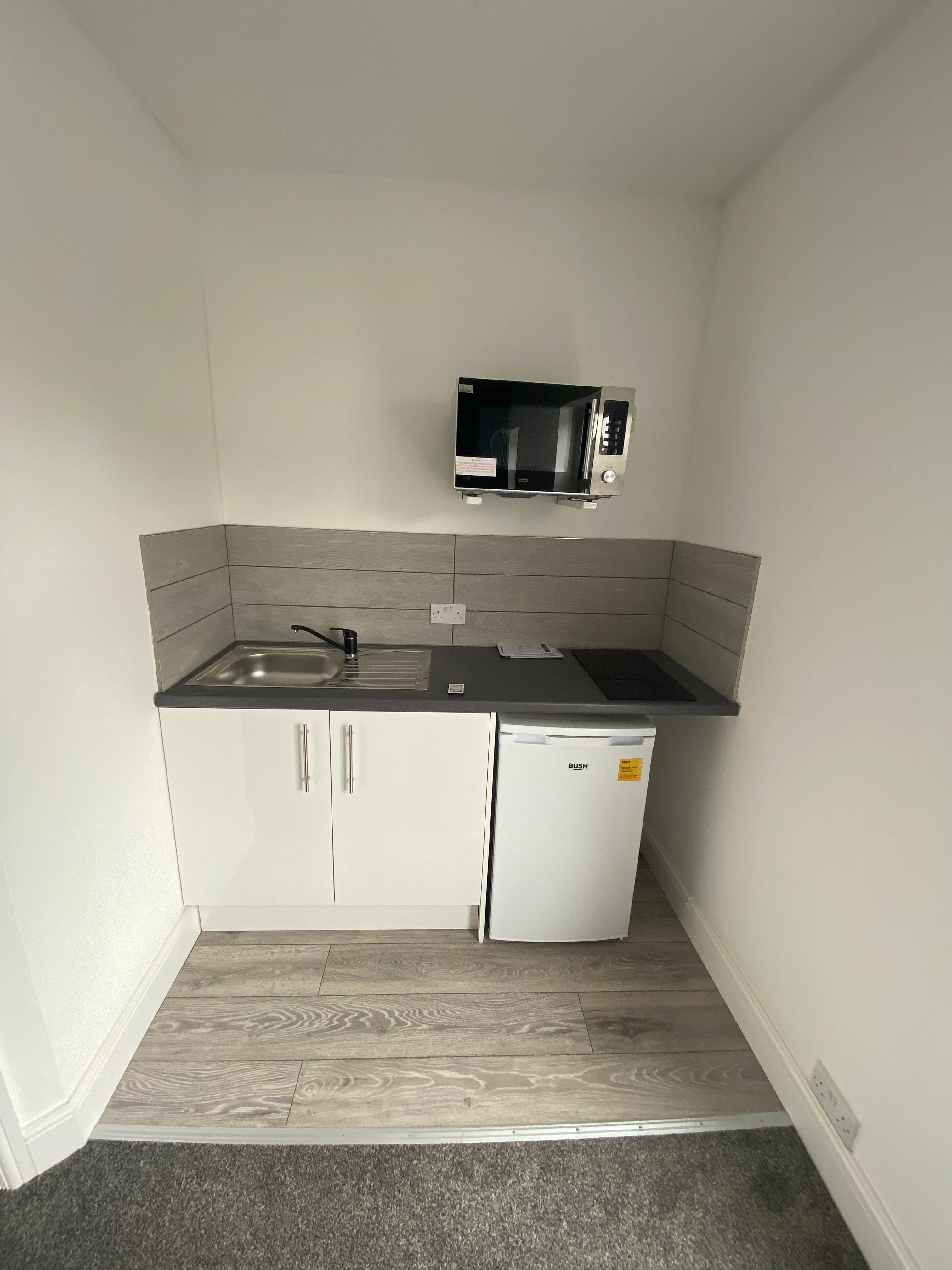 Completed compact rental kitchenette with white units, black worktop and wood-effect flooring