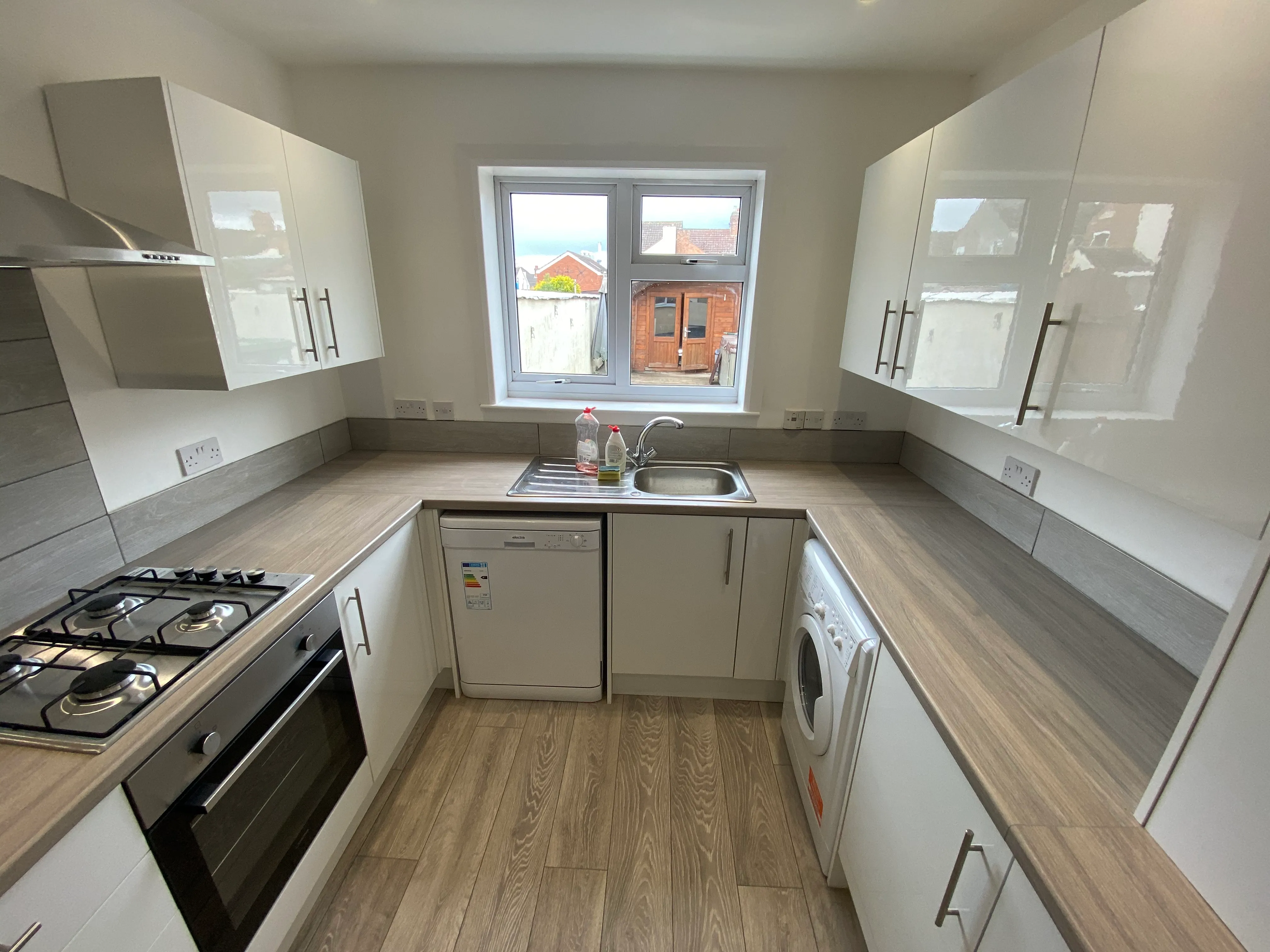 Completed white kitchen refurbishment with integrated appliances and wood-effect flooring